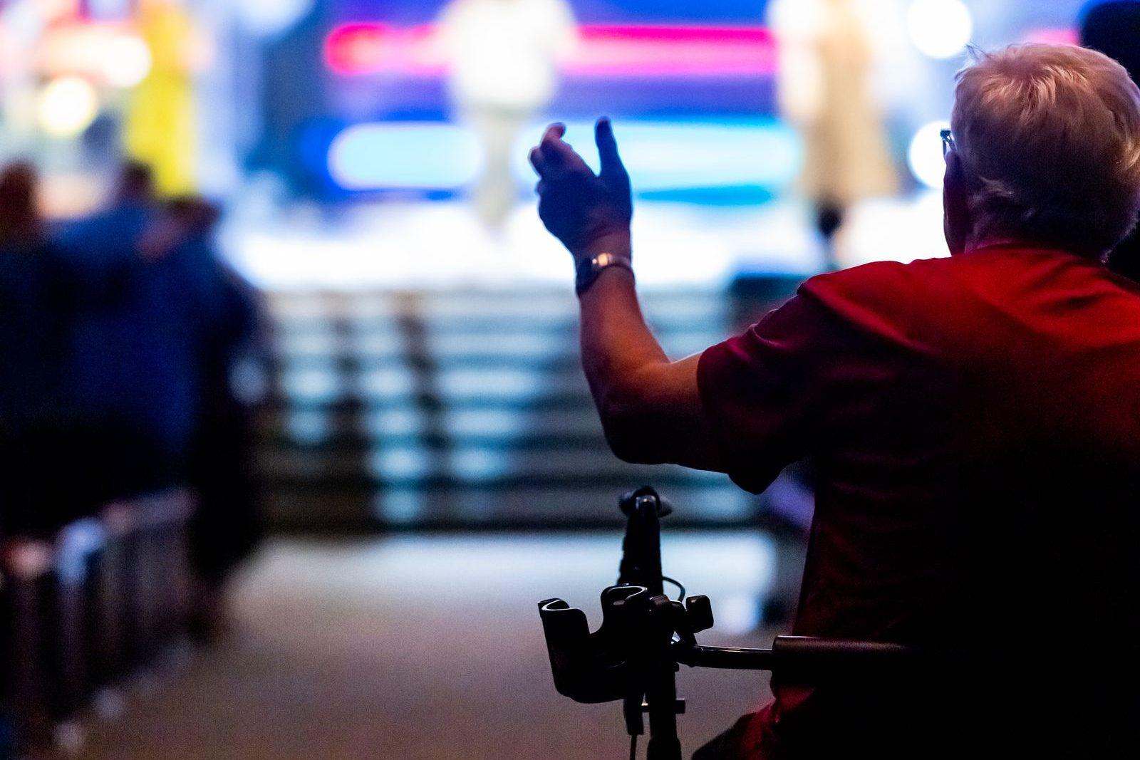 Event attendee using a wheelchair raising a hand toward a brightly lit stage