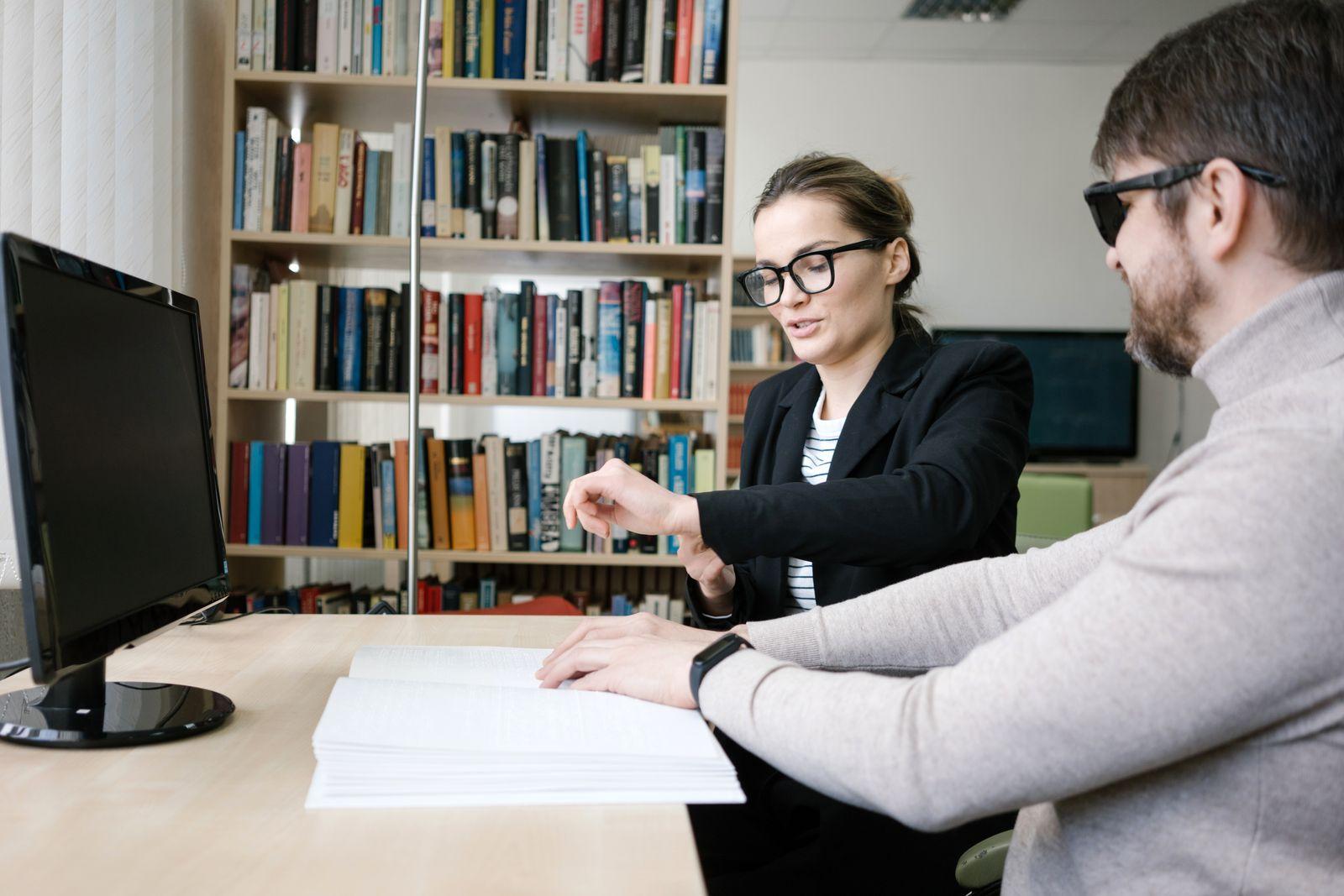 Librarian helping a blind reader access a document through braille