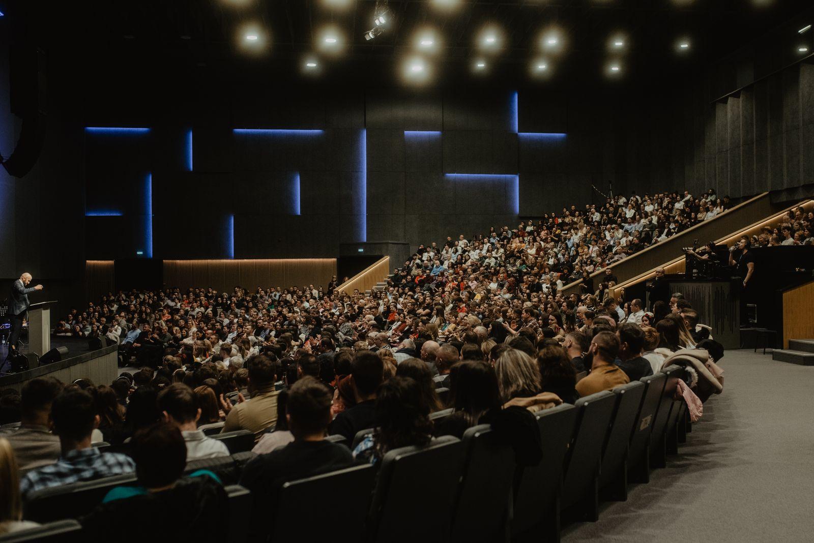 Large audience seated in a conference hall listening to a speaker