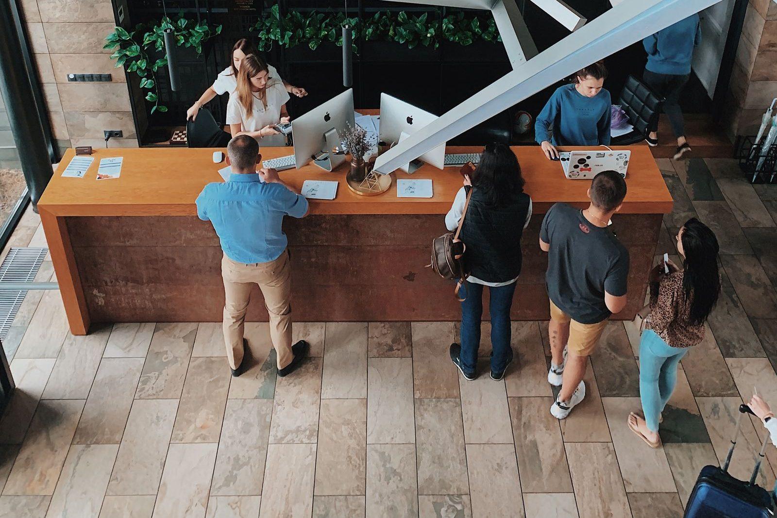 Group of travellers with luggage checking in at a hotel reception desk, seen from above