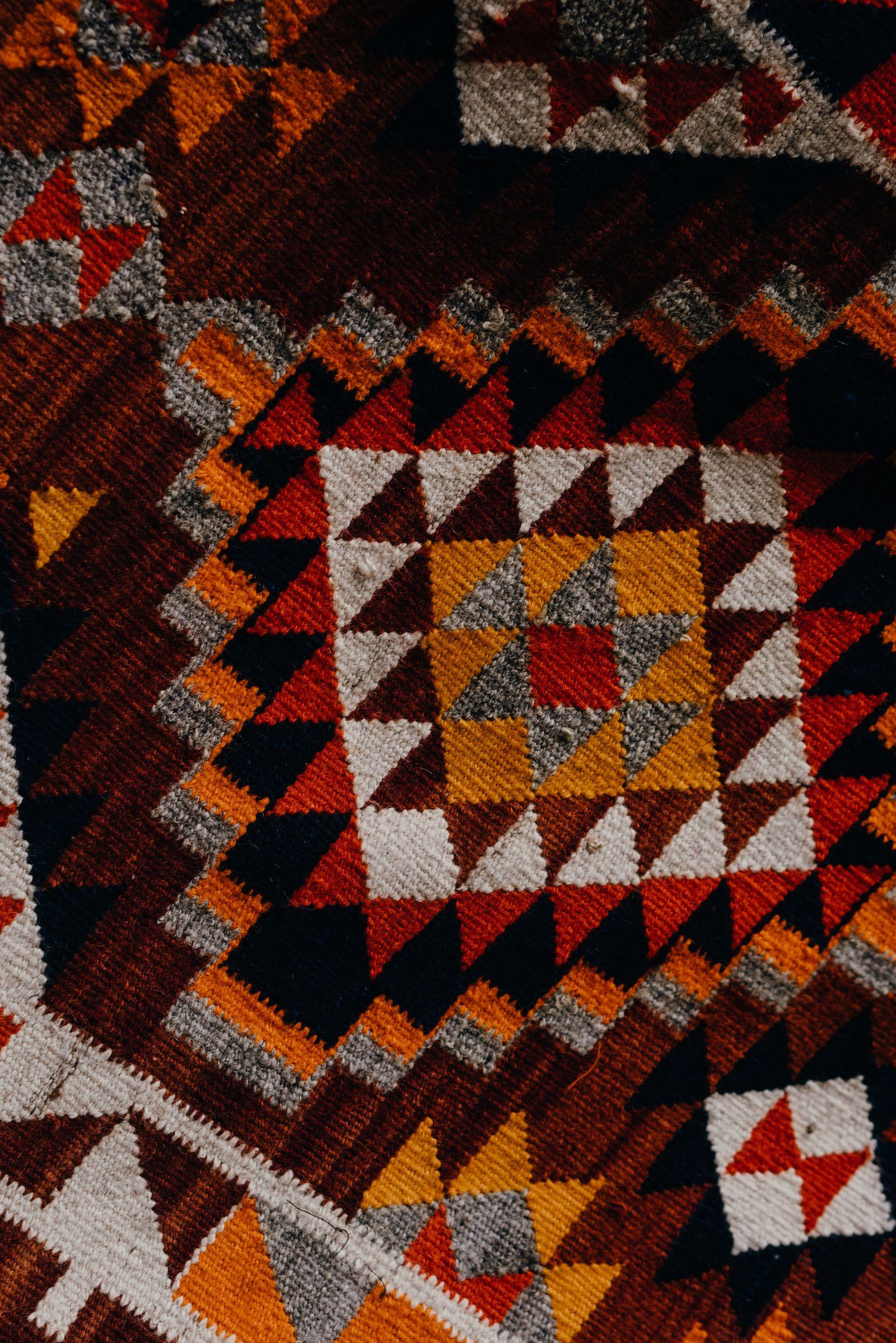 A handwoven wool textile with geometric diamond and triangle patterns in red, gold, cream, and navy — motifs of Southwest weaving.